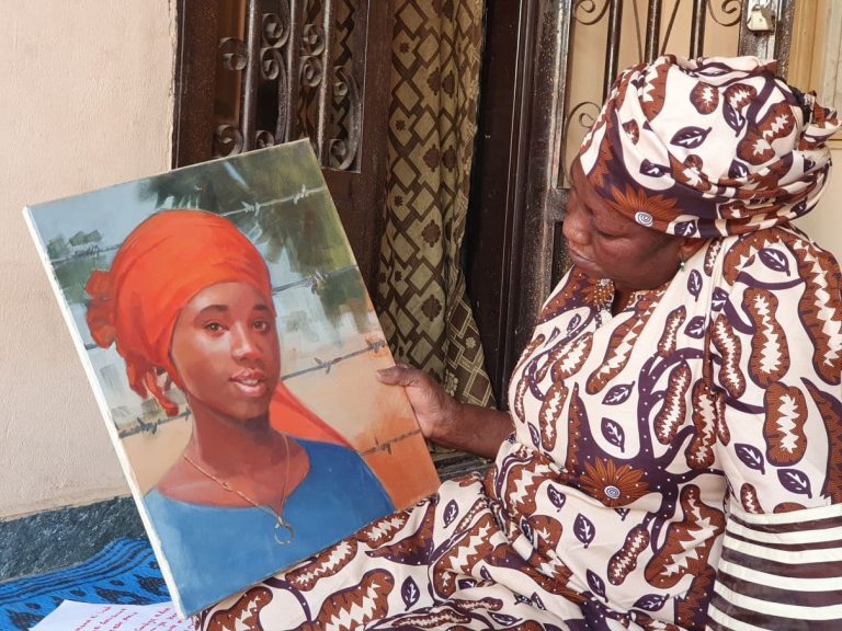 Afrikkalainen nainen katselee käsissään olevaa maalausta nuoresta afrikkalaisesta naisesta.