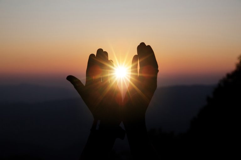 Kädet kohotettuna rukoukseen, aurinko keskellä
