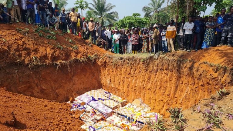 Surevia joukkohaudan äärellä, osittain täytetyssä haudassa näkyy värikkäitä arkkuja.