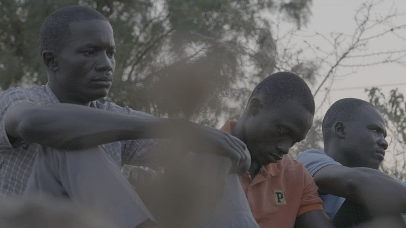 Kolme afrikkalaista miestä istumassa vakava ilme kasvoillaan.