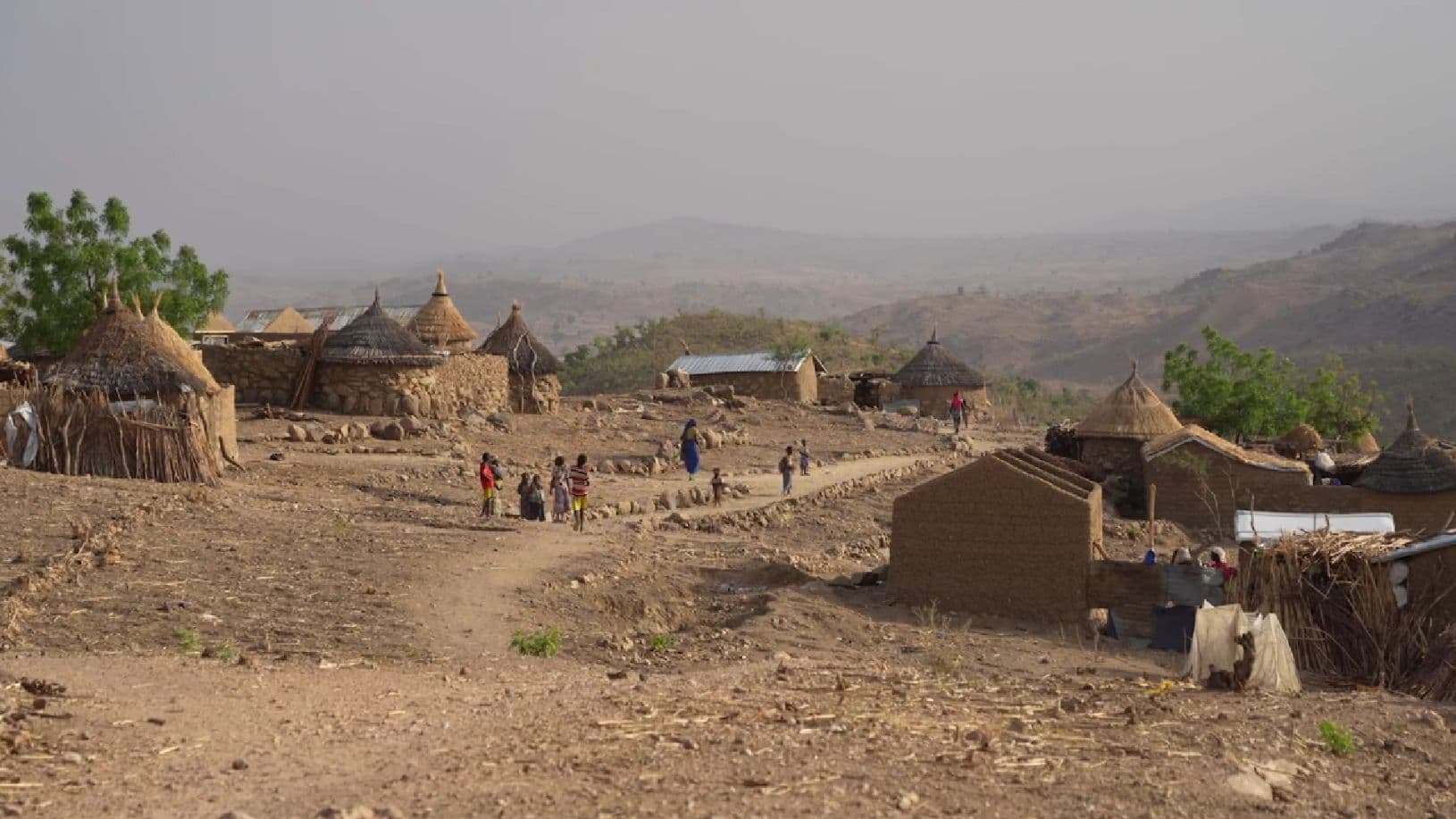 Savimajoja, joiden välissä hiekkainen tie ja tiellä ihmisiä. Tautalla vuoristoista maisemaa.