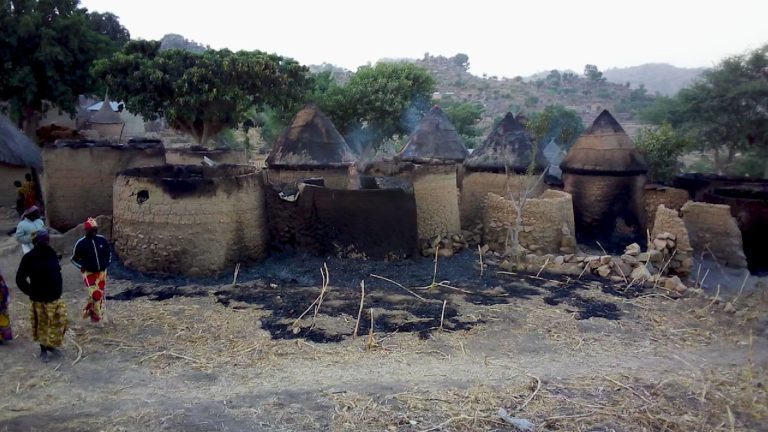 Poltettuja savimajoja, vieressä muutama ihminen katselemassa. Taustalla vuoristomaisemaa.