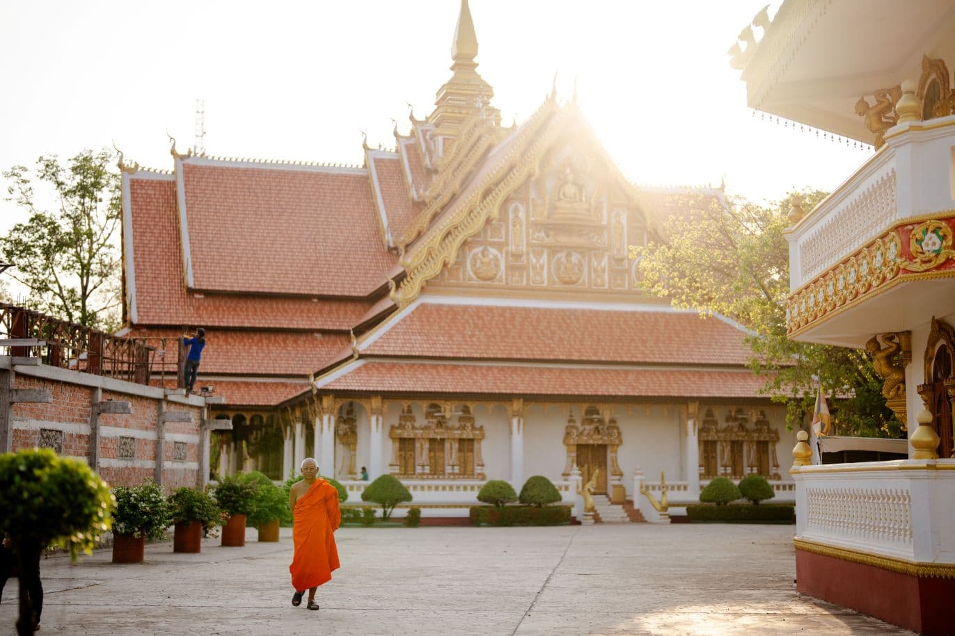 Buddhalainen temppeli ja sen edessä yksi buddhalainen munkki oranssissa kaavussa.