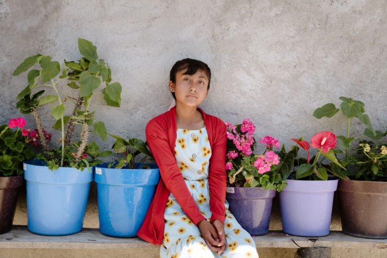 Tyttö istuu ruukkukukkien keskellä.