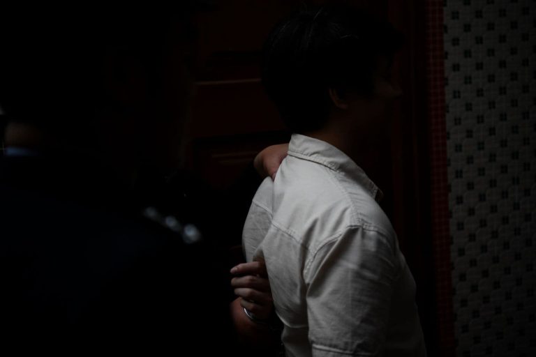 Kädet tarttuvat miehen niskaan ja selkään takaapäin, kummankin ihmisen kasvot jäävät pimeään.