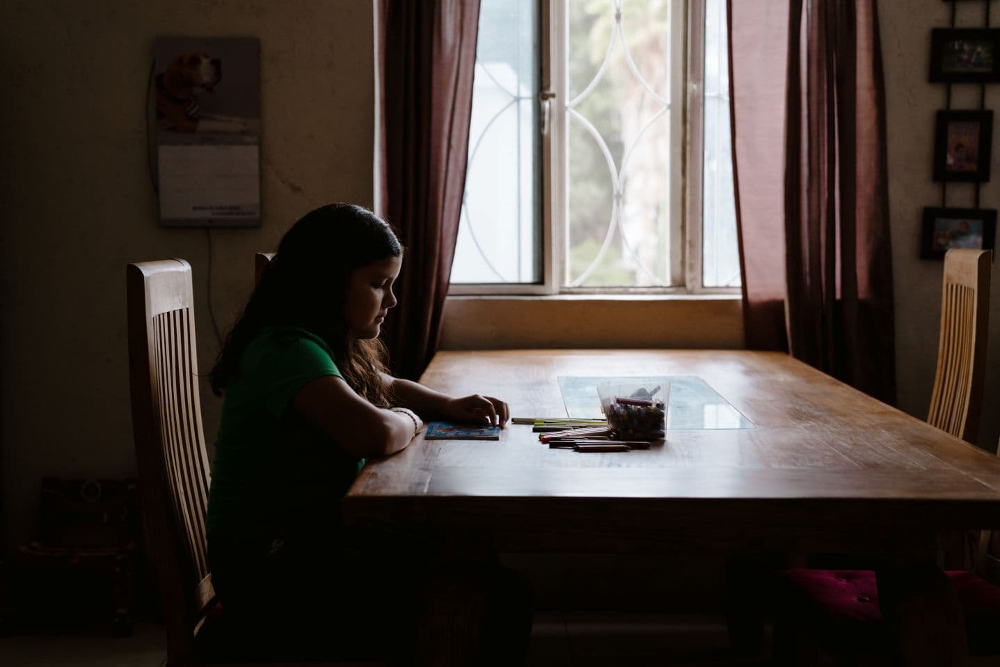 Tyttö istuu pöydän ääressä ikkunan edessä ja värittää paperia.