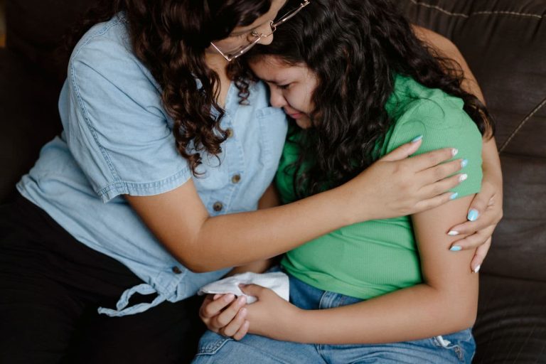 Nainen halaa tyttöä, jolla on kädessään nenäliina.