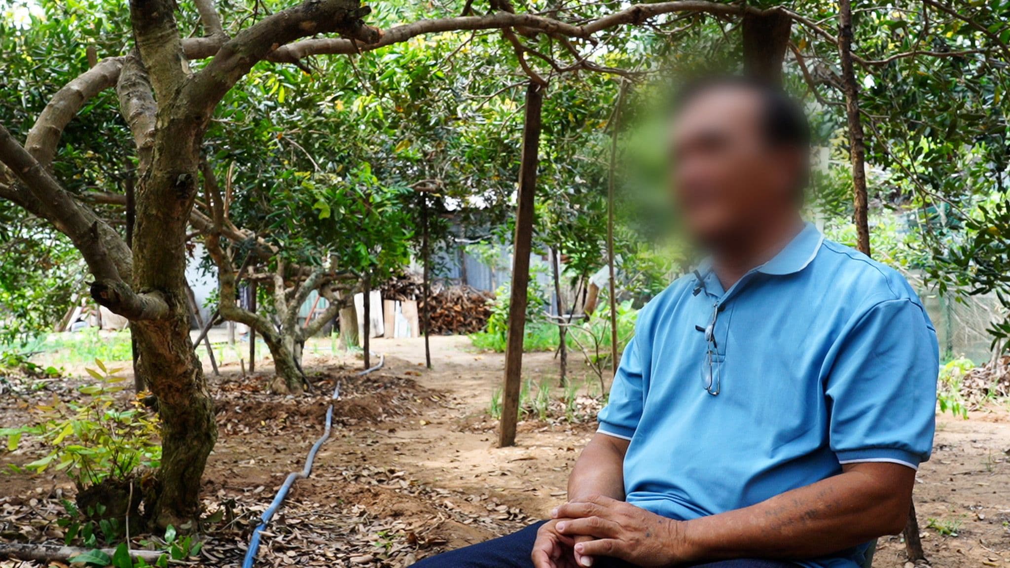 Mies istuu tuolilla ulkona, ympärillä puita. Miehen kasvot on sumennettu.