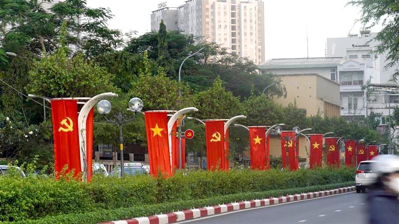 Katu, jonka varrella roikkuu pylväistä punaisia lippuja, joka toisessa lipussa on keltainen tähti, joka toisessa sirppi ja vasara. Taustalla kerrostaloja.