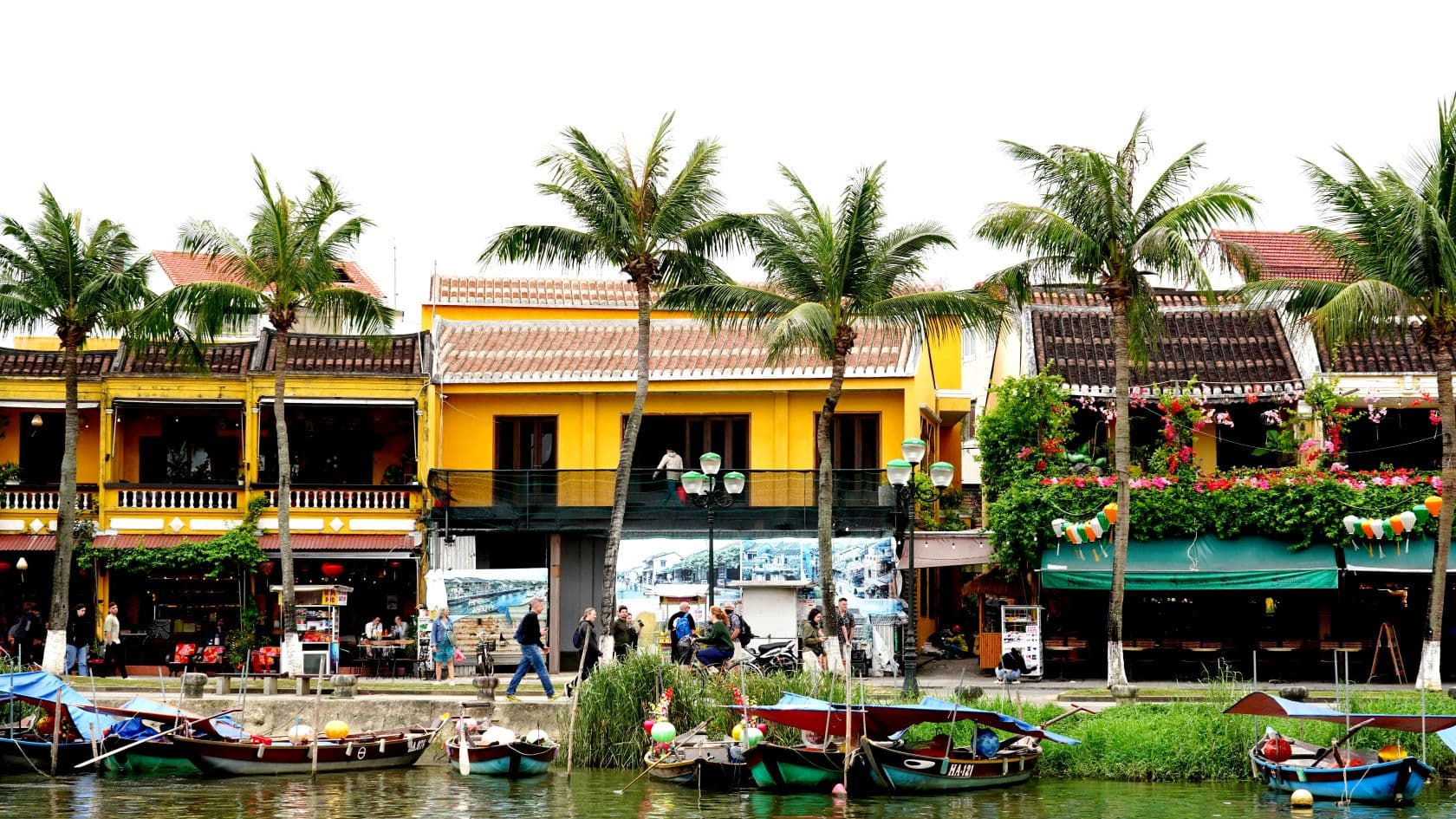 Joelta päin otettu kuva joen rannasta, jossa veneitä. Taustalla rakennuksia, rakennusten ja veden välissä rantakatu.