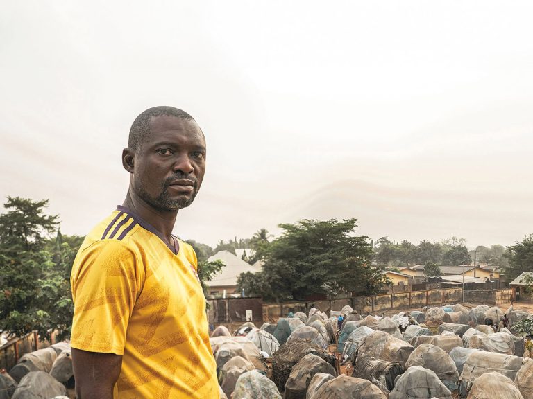 Nigerialainen mies pakolaisleirin pressuasumukset taustalla