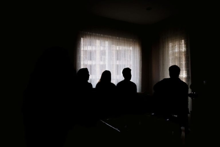 Ihmisten siluetteja tummassa huoneessa ikkunaa vasten.