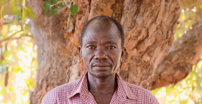 Afrikkalainen mies, taustalla paksurunkoinen puu.