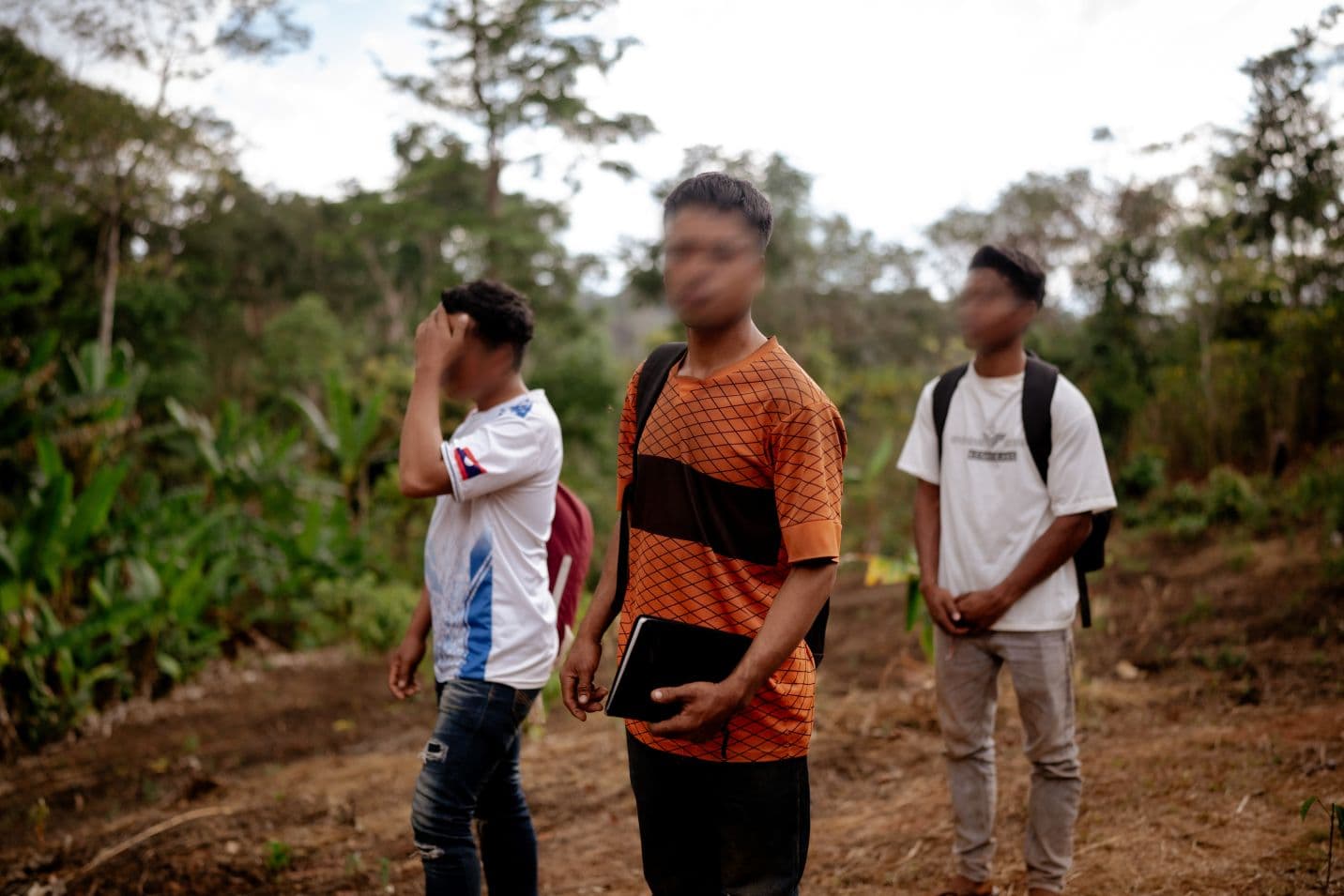 Kolme miestä, joiden kasvot on sumennettu, seisoo aukealla, taustalla viidakkoa.