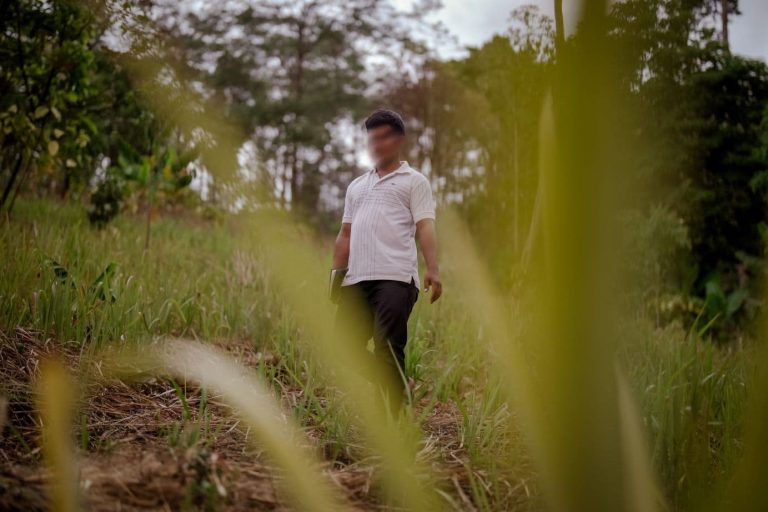 Mies seisoo heinikkoisessa rinteessä Raamattu kädessä, kasvot sumennettuina. Taustalla metsää.