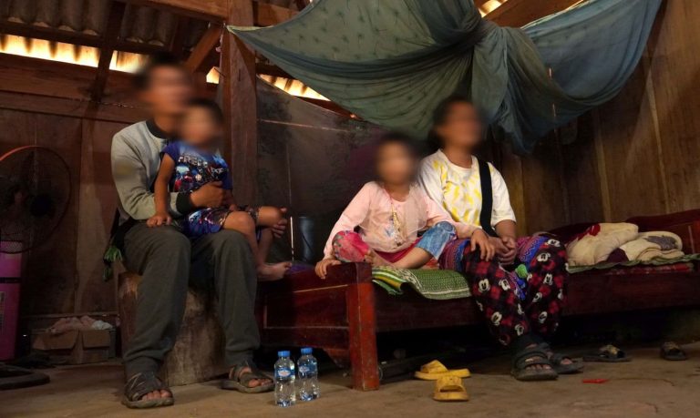 Mies istumassa tuolilla poika sylissään ja nainen ja tyttö istumassa vierekkäin sängyllä. Ihmisten kasvot on sumennettu.