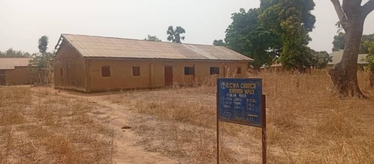 Matala yksikerroksinen rakennus, jonka ympärillä kuivunutta heinikkoista maata ja muutama puu.