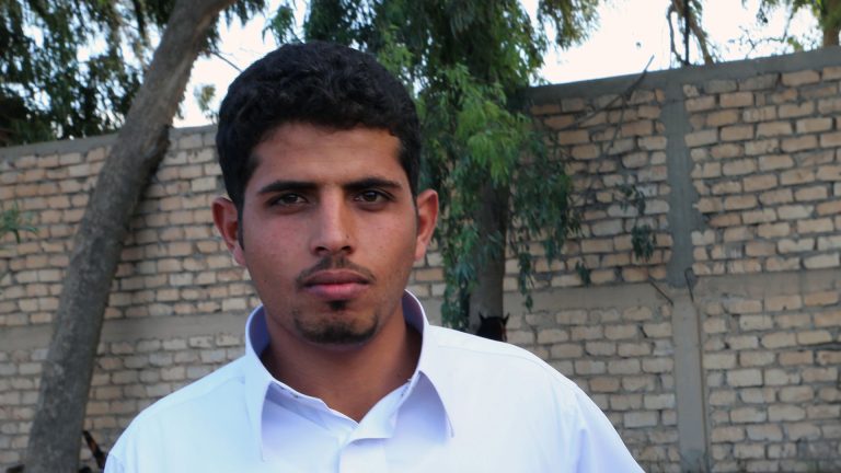 Nuori mies, taustalla tiilimuuri ja puita.