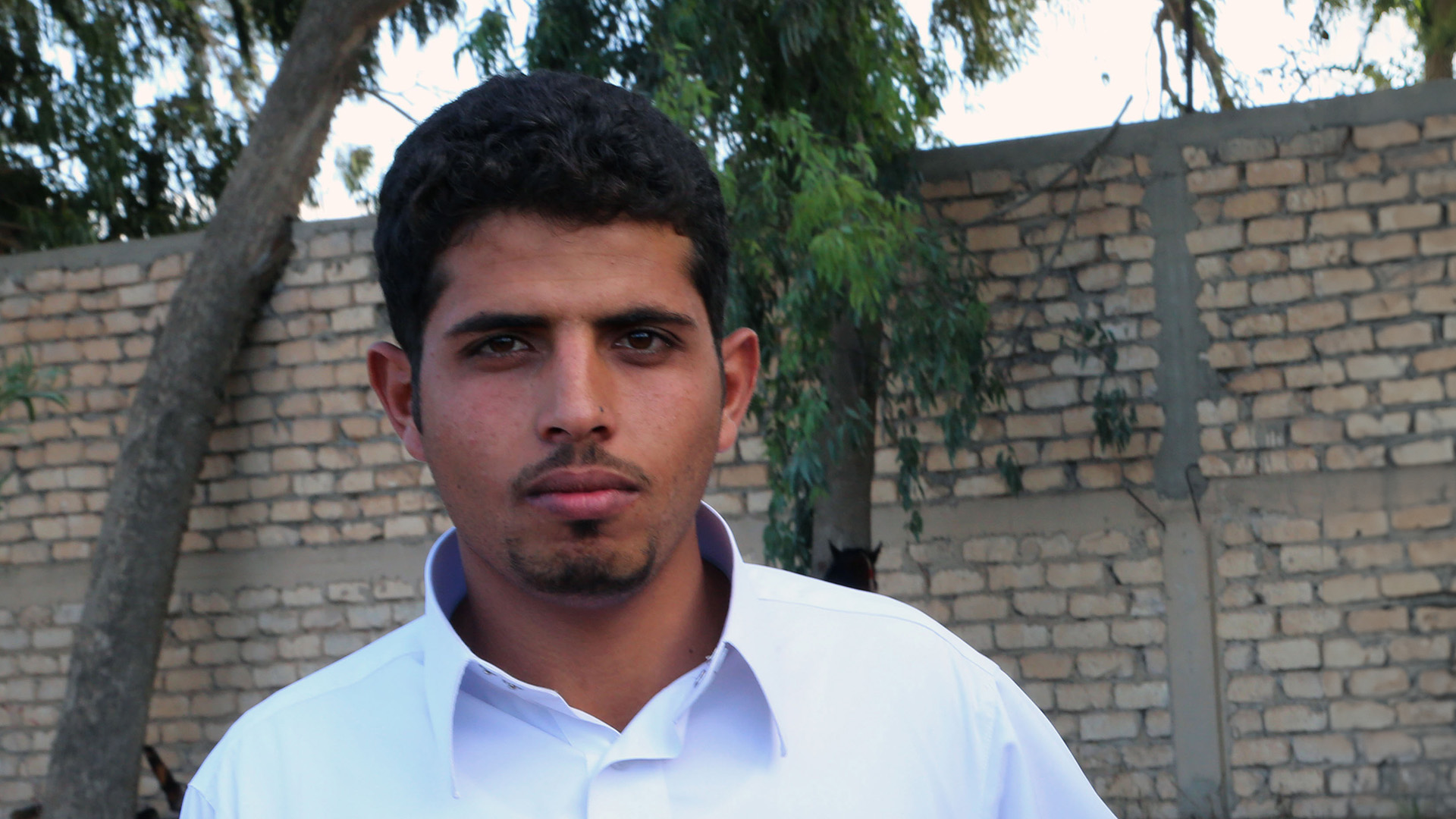 Nuori mies, taustalla tiilimuuri ja puita.