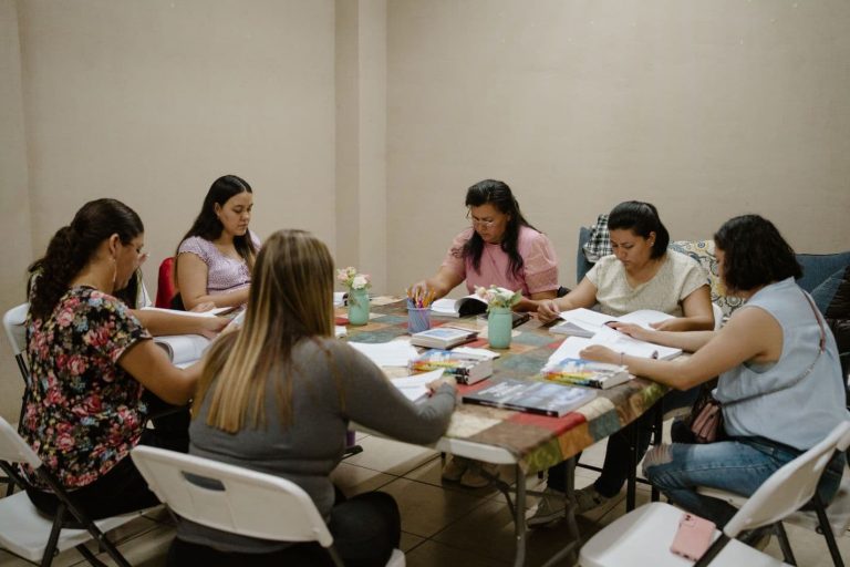 Pöytä, jonka äärellä istuu kuusi naista lukemassa kirjoja. Pöydällä kirjoja sekä muistiinpanovälineitä.